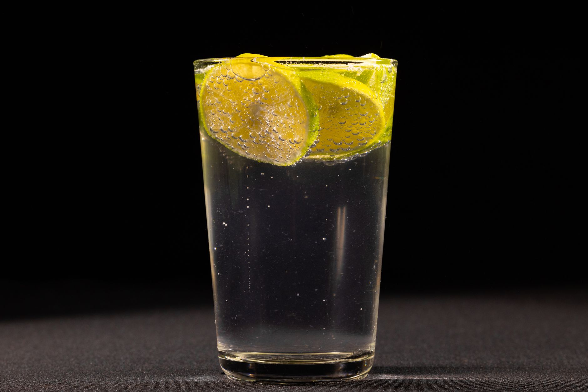 A tall vodka soda over ice with fresh lime slices on a dark background